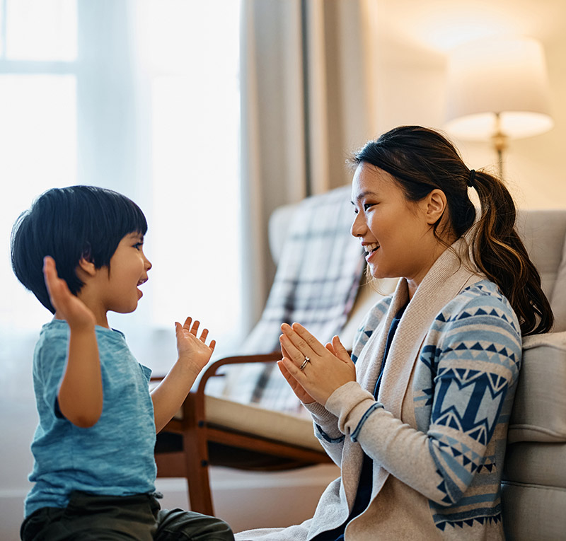Happy Asian kid and his mother have fun while playing clapping game at home.